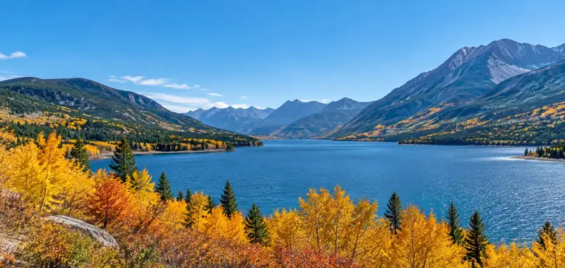 Blue mountain lake framed by forested peaks and golden autumn trees